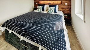 Un lit bien fait, avec une couvre-lit à motifs, une tête de lit en bois et une table de chevet sur laquelle se trouve une horloge.