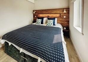 A neatly made bed with a patterned bedspread, a wooden headboard, and a bedside table with a clock.