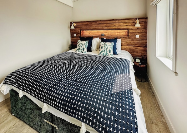 A neatly made bed with a patterned bedspread, a wooden headboard, and a bedside table with a clock. - 2 bedroom accommodation in Tewkesbury (Tewkesbury)