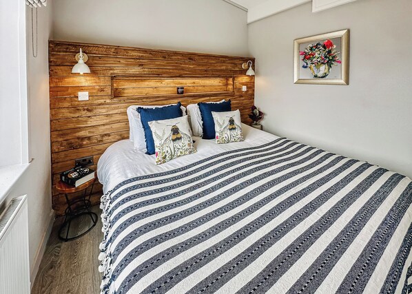 A bedroom with a wooden headboard, a striped bedspread, and a framed floral artwork on the wall.