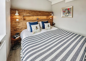 Un dormitorio con cabecera de madera, colcha a rayas y una obra de arte floral enmarcada en la pared.