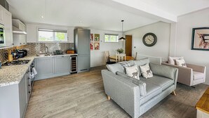 Une cuisine moderne avec des meubles gris, un four encastré et un coin repas comprenant un canapé gris et une table ronde.