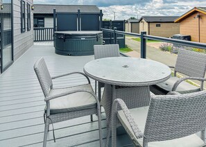 Un espacio al aire libre techado con mobiliario de mimbre, un jacuzzi y vistas de los edificios circundantes.