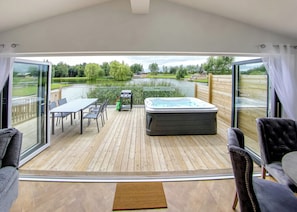 Una terraza con jacuzzi, mesa, sillas y vistas a un lago y follaje.