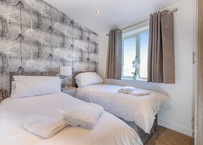 Ett hotellrum med två sängar, ett nattduksbord med en lampa, ett fönster med gardiner och en vägg med ett trädmönster.