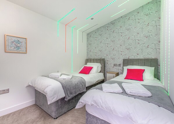 A hotel room with two beds, a small bedside table, a nightstand, a wall-mounted power outlet, and a framed picture on the wall.