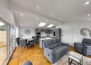 A modern living space with a dining area, sofa, and kitchen.