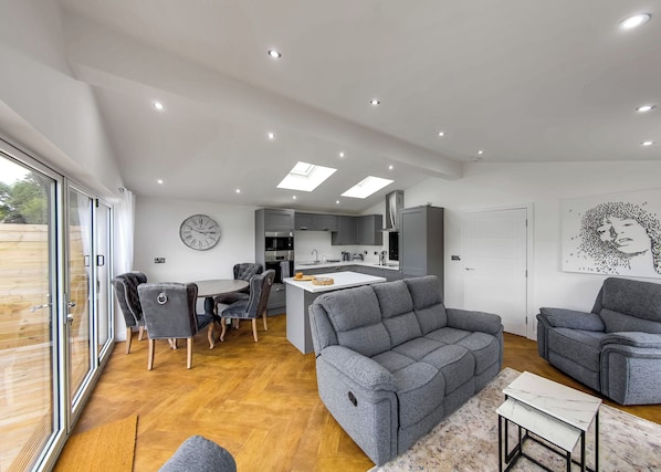 A modern living space with a dining area, sofa, and kitchen.