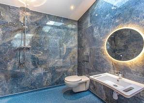 Un baño moderno con pared de mármol, cabina de ducha de vidrio, inodoro y lavamanos con espejo.
