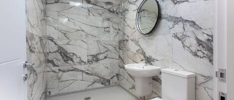 A bathroom with marble walls, a shower, a sink, and a toilet.