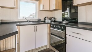 A compact kitchen with a window, a stove, an oven, and a toaster. - Large 12ft-wide caravan with one double with en suite W. (Cardigan)