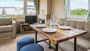 A dining area with a wooden table set for four, a television, and a view of houses through the window. - Large 12ft-wide caravan with one double with en suite W. (Cardigan)