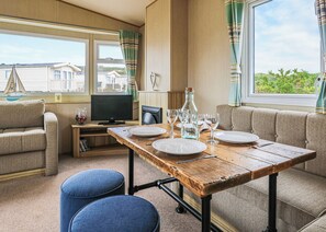 A dining area with a wooden table set for four, a television, and a view of houses through the window.