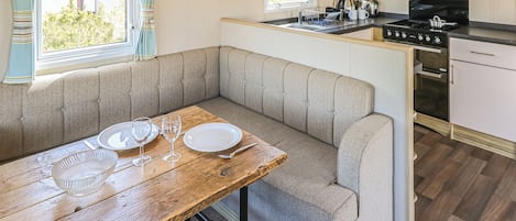A compact kitchen with a dining area, including a bench, a table with dishes and glasses, and a stove.