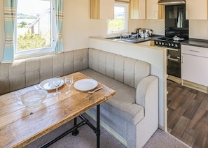 A compact kitchen with a dining area, including a bench, a table with dishes and glasses, and a stove.