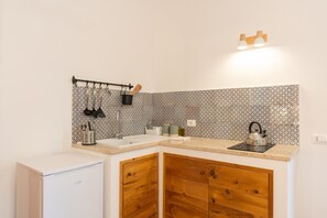Une cuisine compacte équipée d’un évier, de placards en bois, d’une bouilloire et d’un porte-ustensiles fixé au mur.