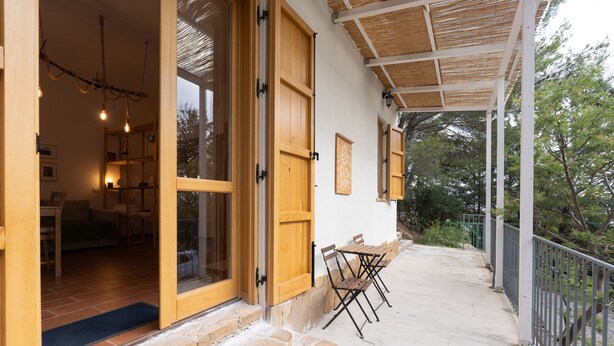 A wooden exterior with a stone-paved entrance, a covered outdoor seating area, and a view of the surrounding trees.