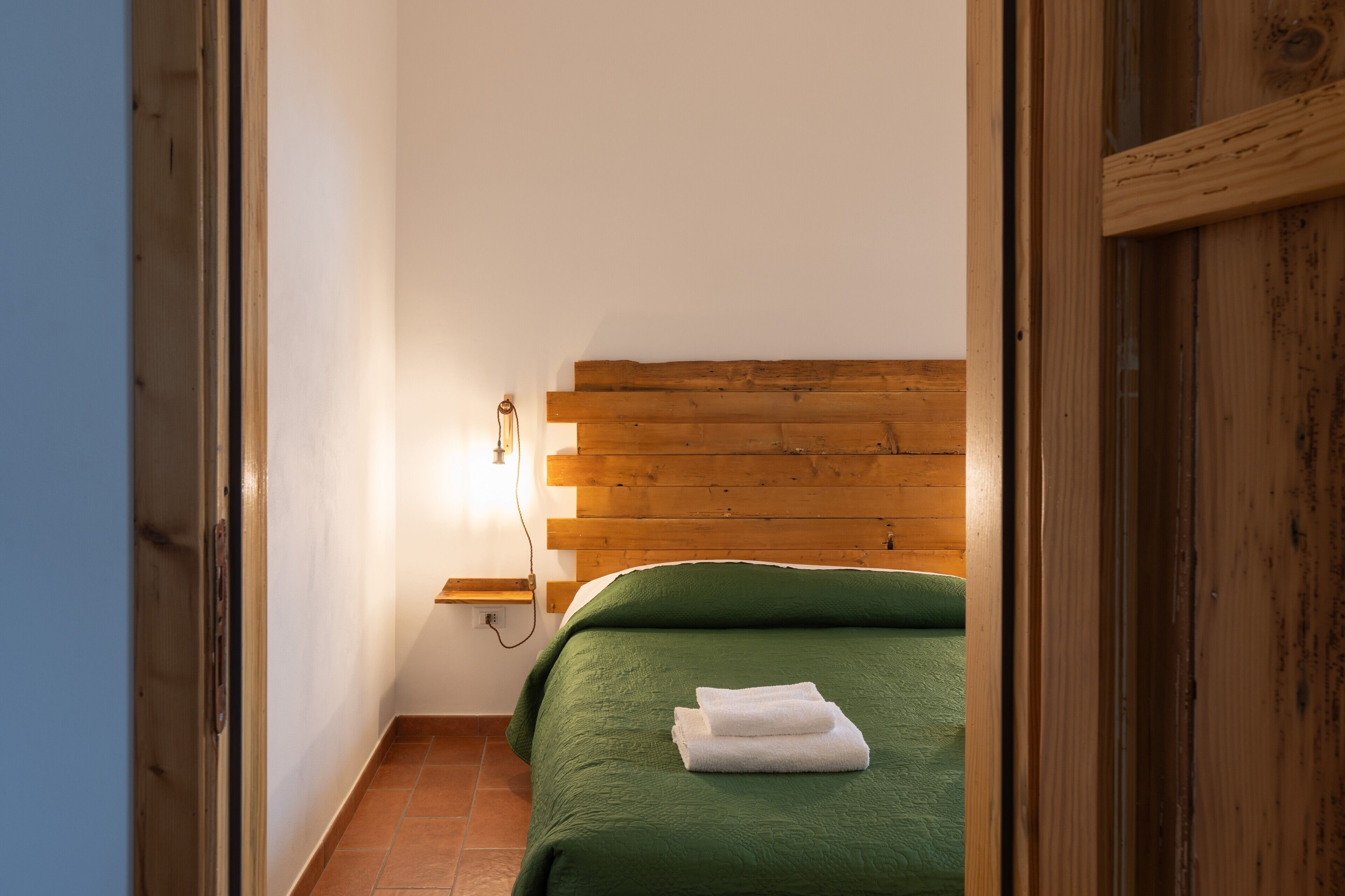 Een slaapkamer met een houten hoofdeinde, groene beddengoed en een nachtkastje met een lamp.