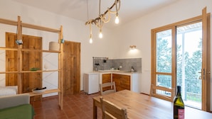 A compact kitchen with a dining table, wooden shelves, and a view through a glass door.