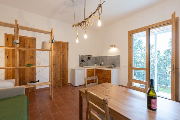 Une cuisine compacte avec une table à manger, des étagères en bois et une vue à travers une porte vitrée.