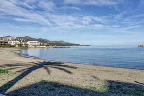 A beach with a pebbly shore, a clear sky, and distant mountains.