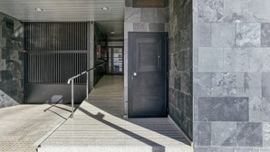 Une entrée moderne, avec une rambarde en métal, une porte sombre et un mur de pierre portant le numéro « 28 ».