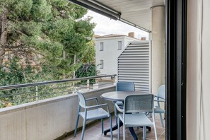 A balcony with a table and chairs, a railing, and a view of trees and buildings.