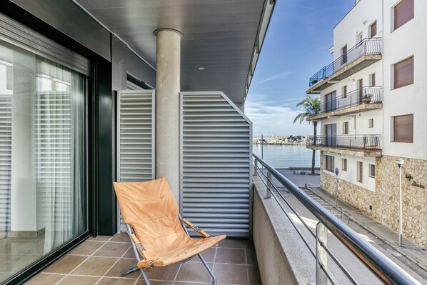 A balcony with a single chair, a view of the sea, and a building with balconies.