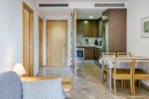 A modern apartment with a dining area, kitchen, and a living room with a sofa and lamp.