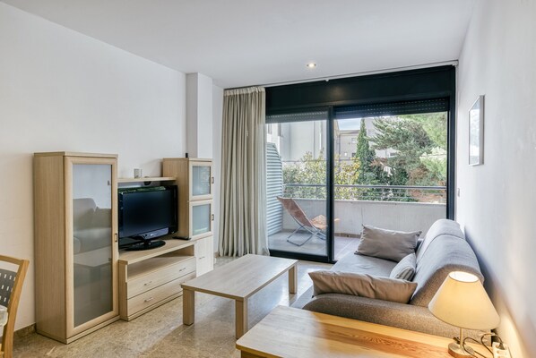 A modern living room with a flat-screen TV, a sofa, a coffee table, and a balcony with a chair.