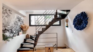 Un intérieur moderne avec un escalier en colimaçon, une grande fenêtre et une œuvre d’art abstraite accrochée au mur.