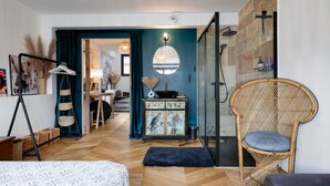 Une chambre à coucher moderne avec un lit, une chaise en osier, une commode et un espace douche.