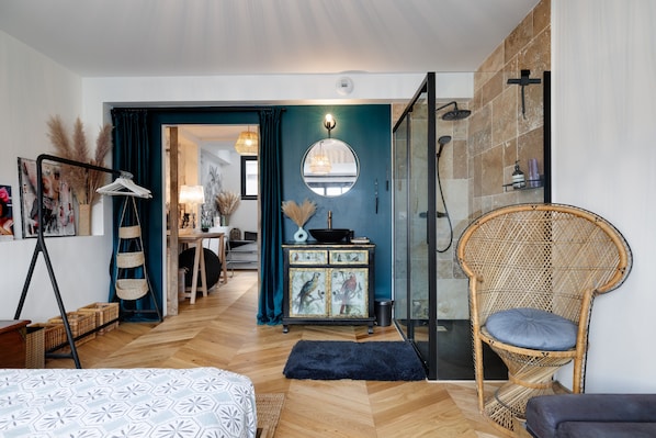 Une chambre à coucher moderne avec un lit, une chaise en osier, une commode et un espace douche.