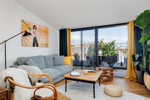 Un salon moderne avec un canapé, une table basse, un fauteuil et une grande fenêtre avec des rideaux.