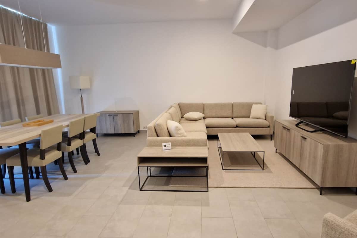 Uma sala de estar moderna com sofá, mesa de centro, televisão e área de jantar.
