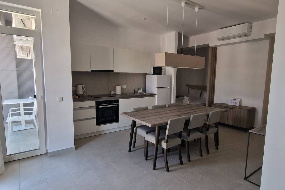 Cozinha moderna com área de jantar, incluindo mesa e cadeiras de madeira, eletrodomésticos embutidos e uma janela grande.