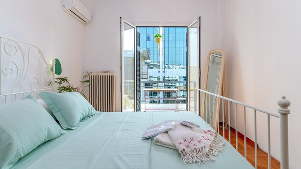 A bedroom with a bed, a hanging plant, a radiator, and a view of the city through an open door. - Apartment 'Dreaming of Greece G1' with Private Terrace, Wi-Fi and Air Conditioning (Athens)