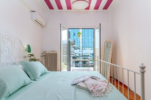 A bedroom with a bed, a hanging plant, a radiator, and a view of the city through an open door. - Apartment 'Dreaming of Greece G1' with Private Terrace, Wi-Fi and Air Conditioning (Athens)