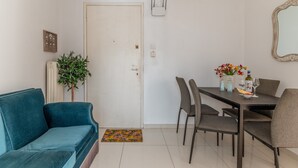 A room with a blue sofa, a dining table with chairs, a potted plant, and a door. - Apartment 'Dreaming of Greece G1' with Private Terrace, Wi-Fi and Air Conditioning (Athens)