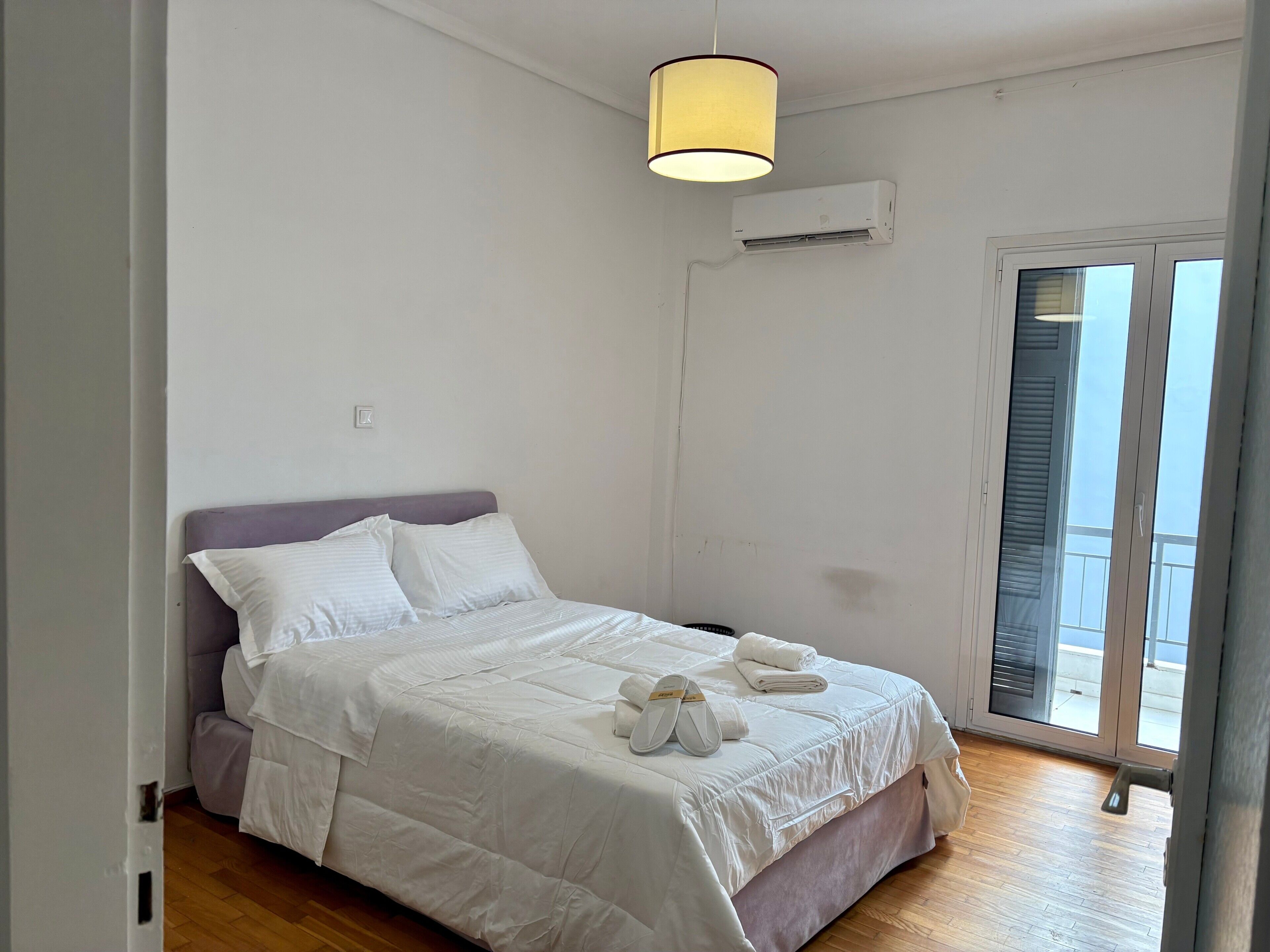 Une chambre à coucher comprenant un lit, un luminaire au plafond, un appareil de climatisation et une porte-fenêtre coulissante donnant sur l’extérieur.