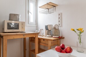 A kitchen with a microwave, coffee maker, and a bowl of fruit on a wooden table.