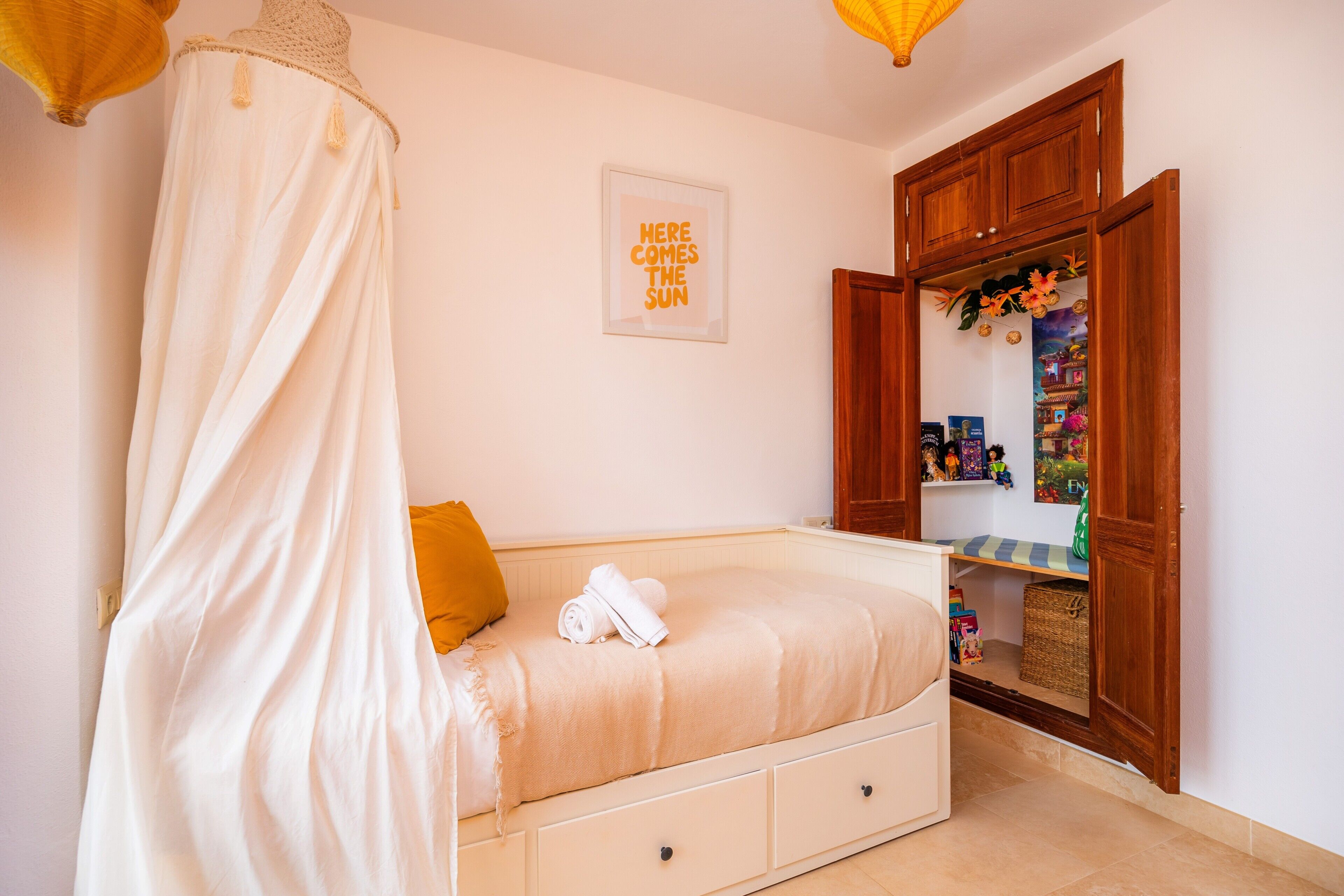 A bedroom with a canopy bed, a small bedside table, a wardrobe, and a framed picture on the wall.