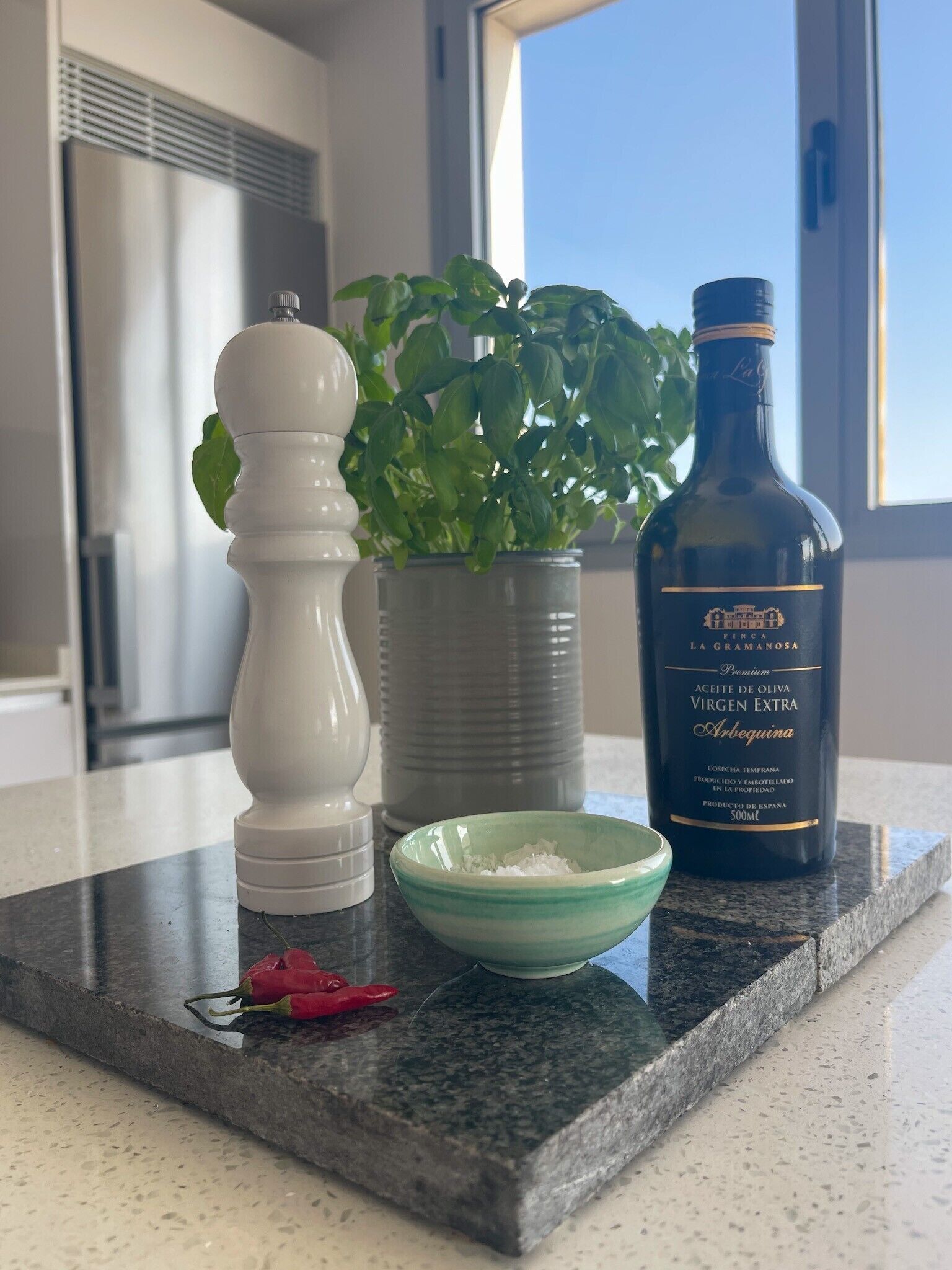 A kitchen counter with a bottle of olive oil, a salt shaker, a pepper shaker, a green bowl, a potted plant, and a red chili pepper.