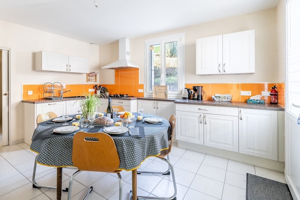 A modern kitchen with white cabinets, a dining table set for four, and a window with a view of greenery.
