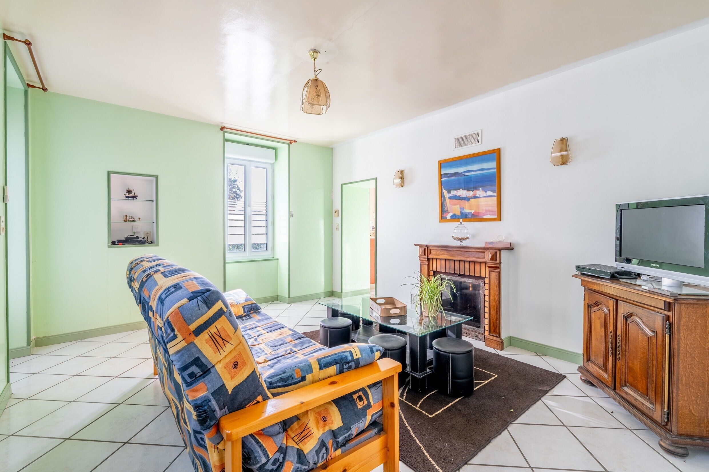 Ein Wohnzimmer mit einer Couch, einem Glastisch, einem Fernseher, einem Kamin und einem Gemälde an der Wand.