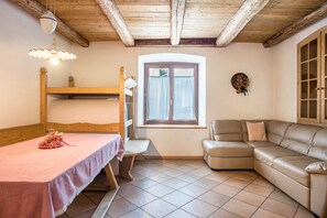 Une pièce avec un lit superposé, un canapé, une table recouverte d’une nappe rose, un banc, une fenêtre avec des rideaux et un plafond en bois.