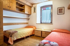 Une chambre avec deux lits, des armoires en bois, une fenêtre avec des rideaux et une petite table.