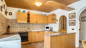 Een keuken met houten kastjes, een betegelde achterwand, een inbouwoven en een keukeneiland met granieten aanrecht.