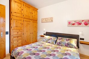 A bedroom with a wooden wardrobe, a bed with patterned bedding, and wall art.