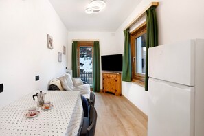 A room with a dining table, chairs, a coffee maker, a TV, a refrigerator, and a wooden cabinet. - Apartment "Arlecchino" with Mountain View, Balcony & Wi-Fi (Livigno)